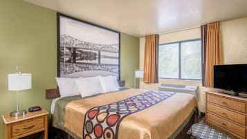 Una camera d'albergo con un letto, una televisione, un comodino, una lampada e una finestra con tende.