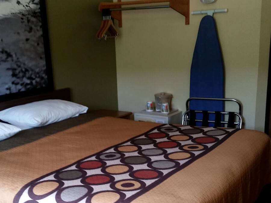 Een hotelkamer met een bed, een wandplank met een strijkplank, een klein tafeltje met een waterkoker en een schilderij aan de muur.