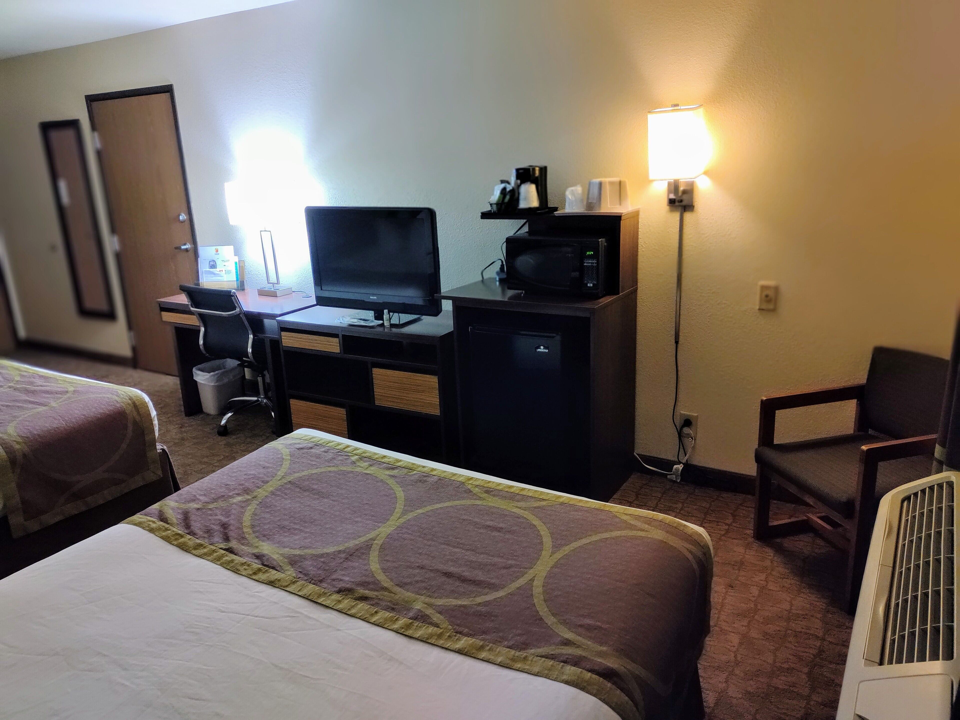 Hotelkamer met twee bedden, een bureau met computer en een magnetron, een stoel en een staande lamp.