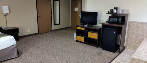 A hotel room with a bed, a desk with a telephone, a television, a small refrigerator, and a microwave.