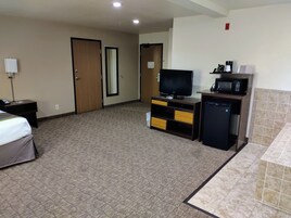 A hotel room with a bed, a desk with a telephone, a television, a small refrigerator, and a microwave.