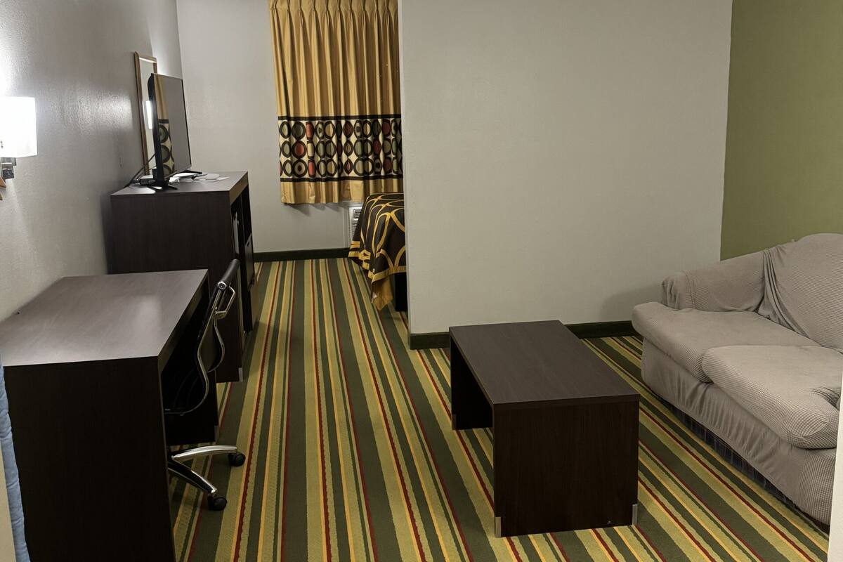 A hotel room with a striped carpet, a desk with a chair, a sofa, and a bed.