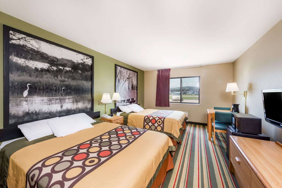 A hotel room with two beds, a TV, a desk, and a window with a view.