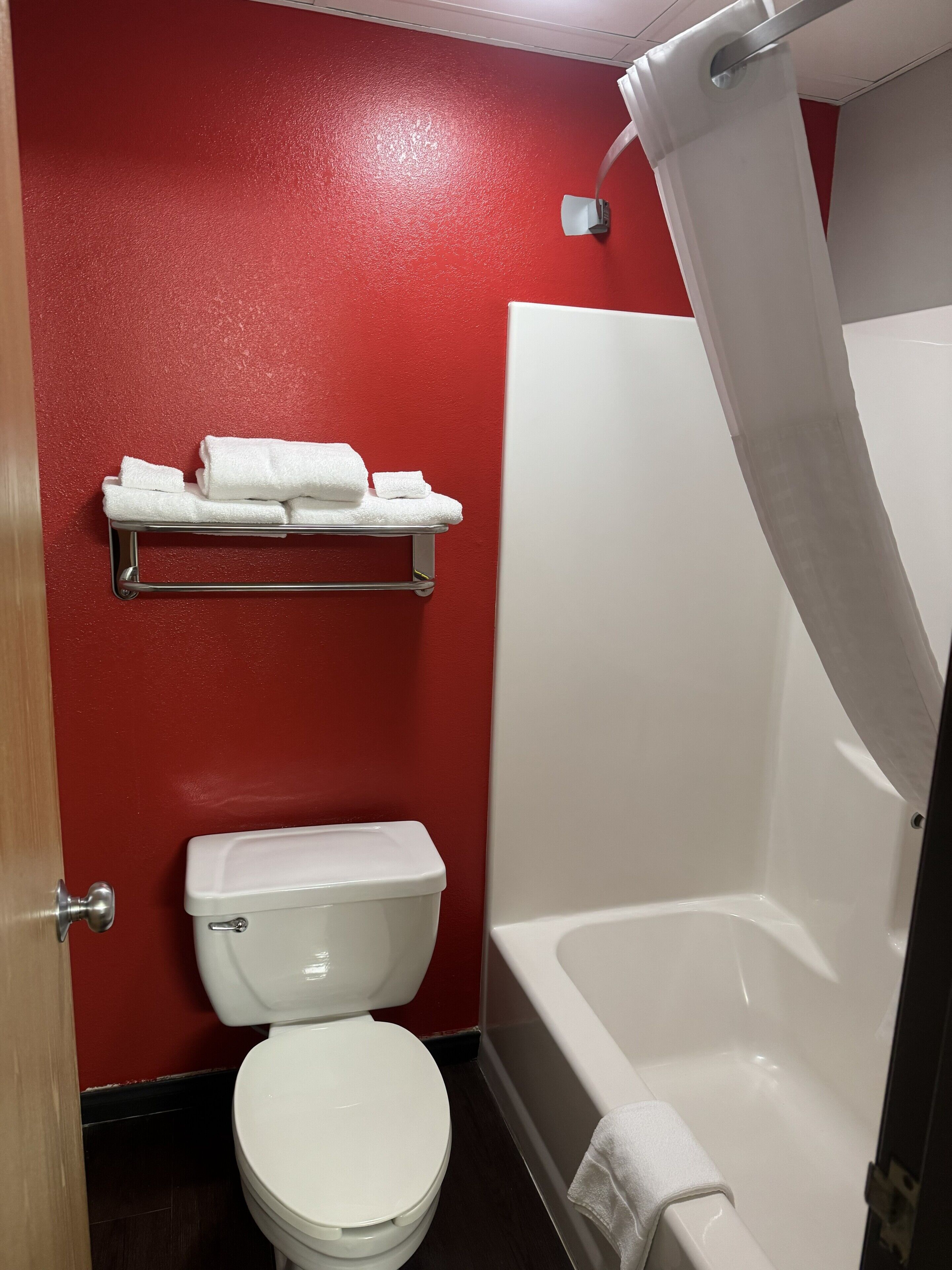 Un baño con una pared roja, un inodoro blanco, una bañera blanca y una cortina de ducha.