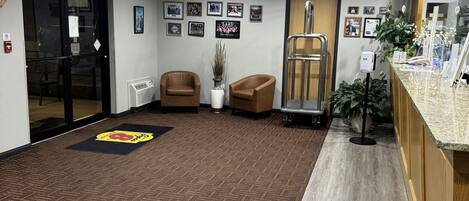 A reception area with a carpeted floor, two leather chairs, a reception desk, a plant, framed pictures on the wall, and an exit sign.
