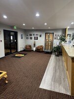 A reception area with a carpeted floor, two leather chairs, a reception desk, a plant, framed pictures on the wall, and an exit sign.