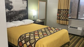 Une chambre d’hôtel comprenant un lit, une table de chevet, une lampe, un miroir, une fenêtre avec des rideaux et un radiateur.