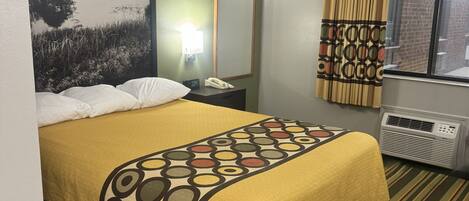 Une chambre d’hôtel comprenant un lit, une table de chevet, une lampe, un miroir, une fenêtre avec des rideaux et un radiateur.