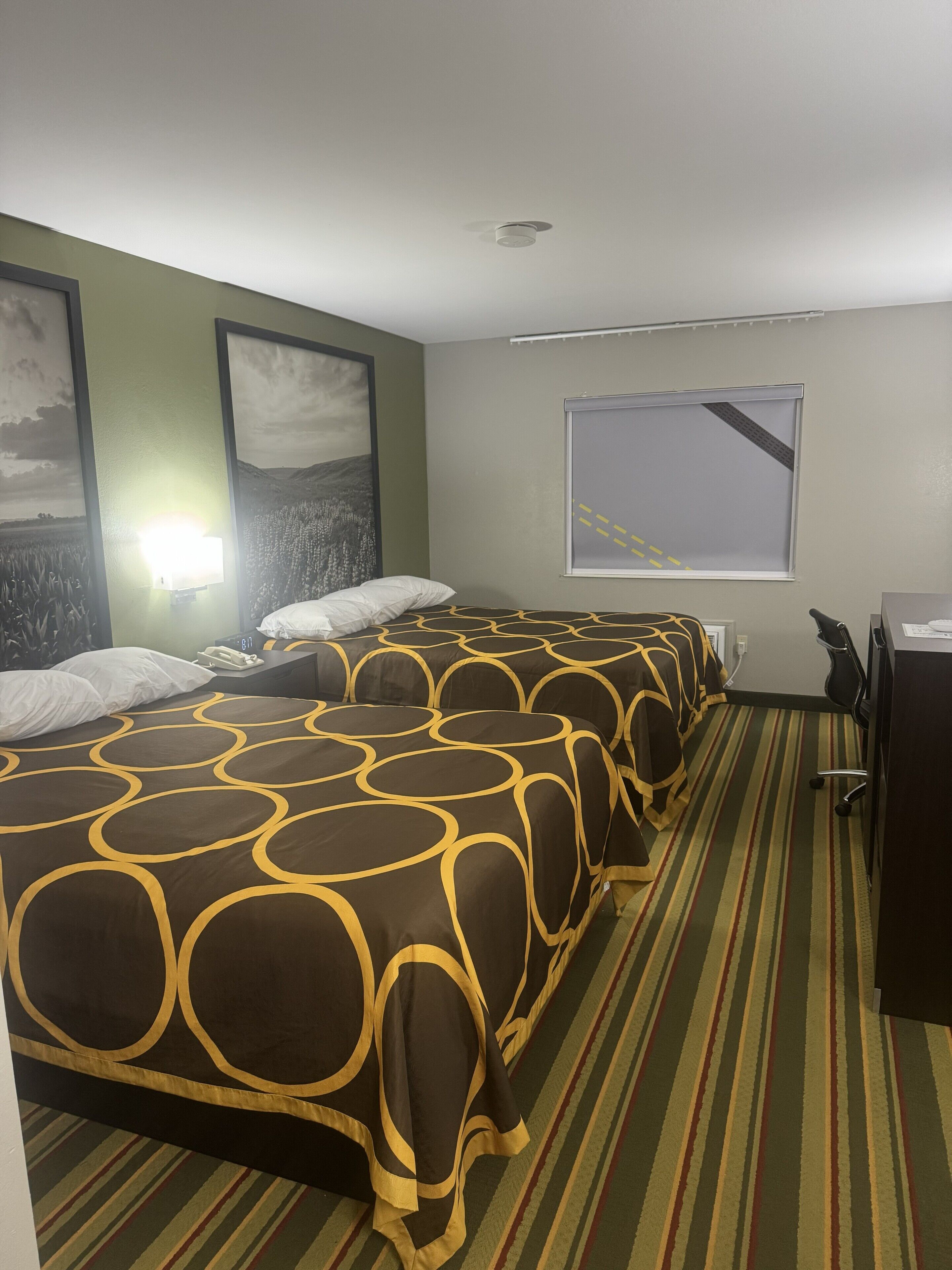 A hotel room with a large bed, a desk, and a window with blinds.