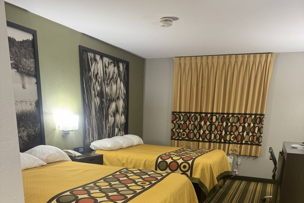A hotel room with two beds, a desk, a chair, a telephone, and a wall-mounted air conditioner.