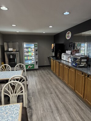 A modern kitchen with a refrigerator, a 7UP vending machine, a microwave, and a breakfast bar. - Super 8 by Wyndham Chanute (Chanute)