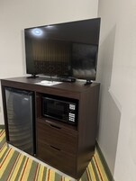 A compact kitchenette with a microwave, refrigerator, and a flat-screen TV on a wooden cabinet.