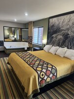 A hotel room with a large bed, a bathroom with a bathtub, a window with curtains, and a wall-mounted mirror.