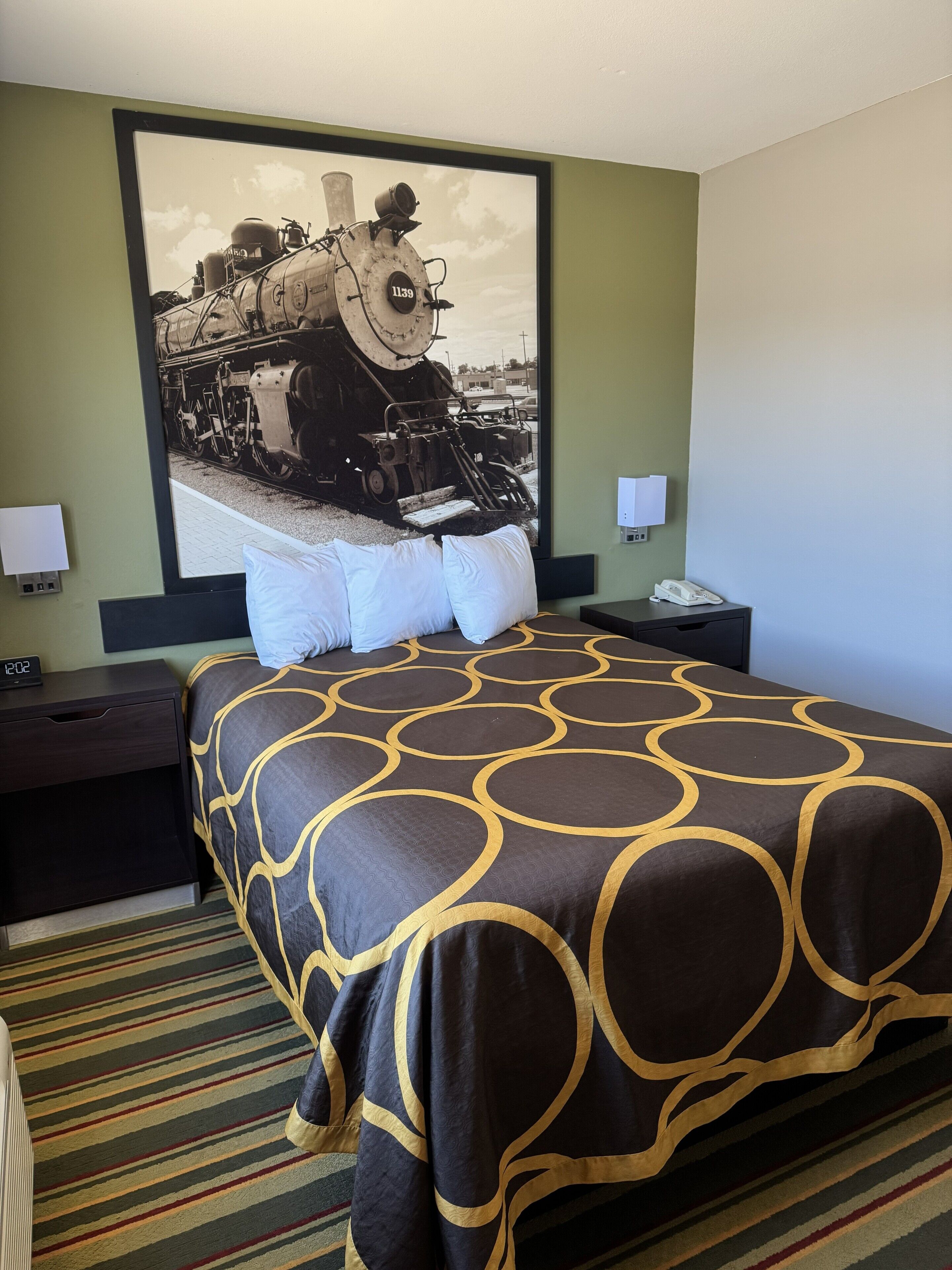 Une chambre d’hôtel avec un grand lit, deux tables de chevet, une horloge et un téléphone fixé au mur.