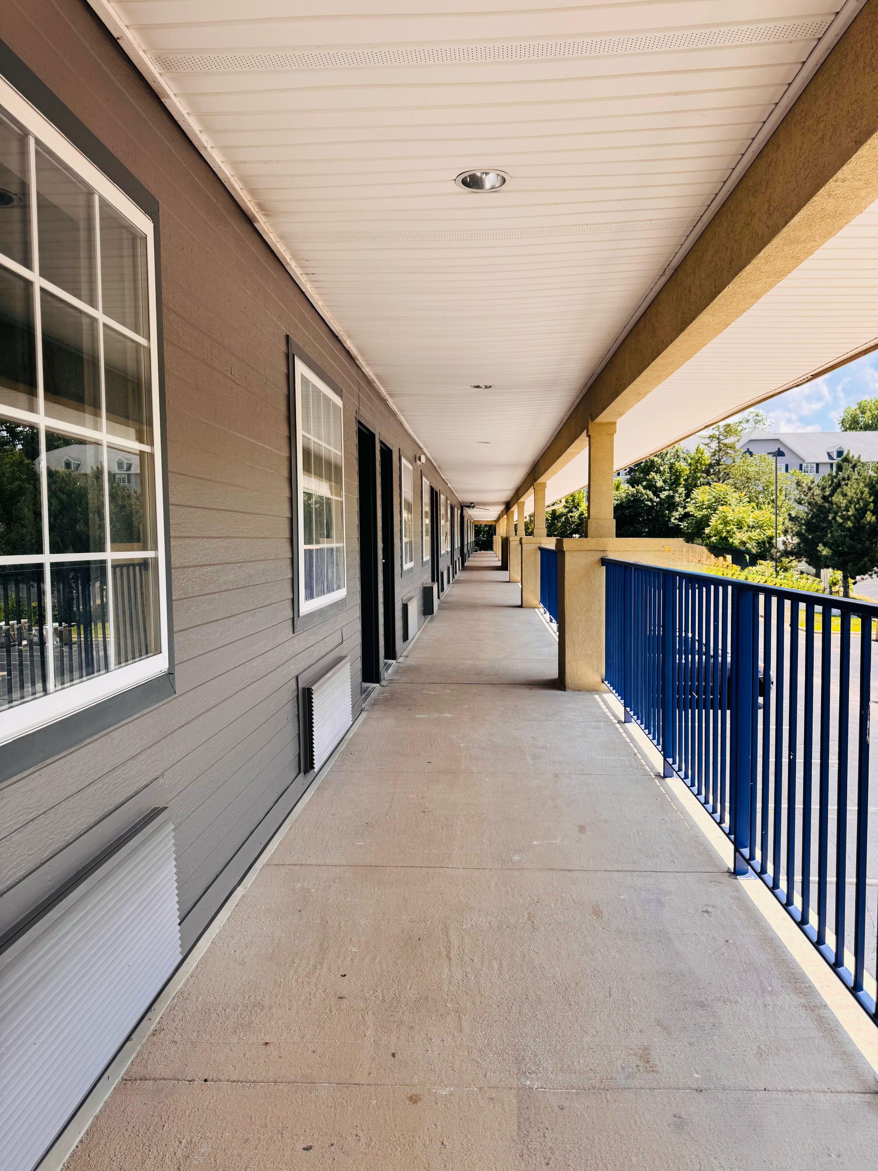 A covered corridor with a concrete floor, large windows, and a blue railing.