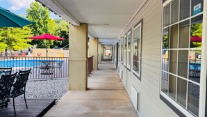 A covered walkway with a pool view, outdoor seating, and a sign for a business. - Wander Inn (Branson)