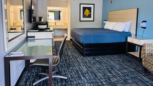 A hotel room with a bed, a desk, a chair, a mirror, a framed picture, and a nightstand. - Wander Inn (Branson)
