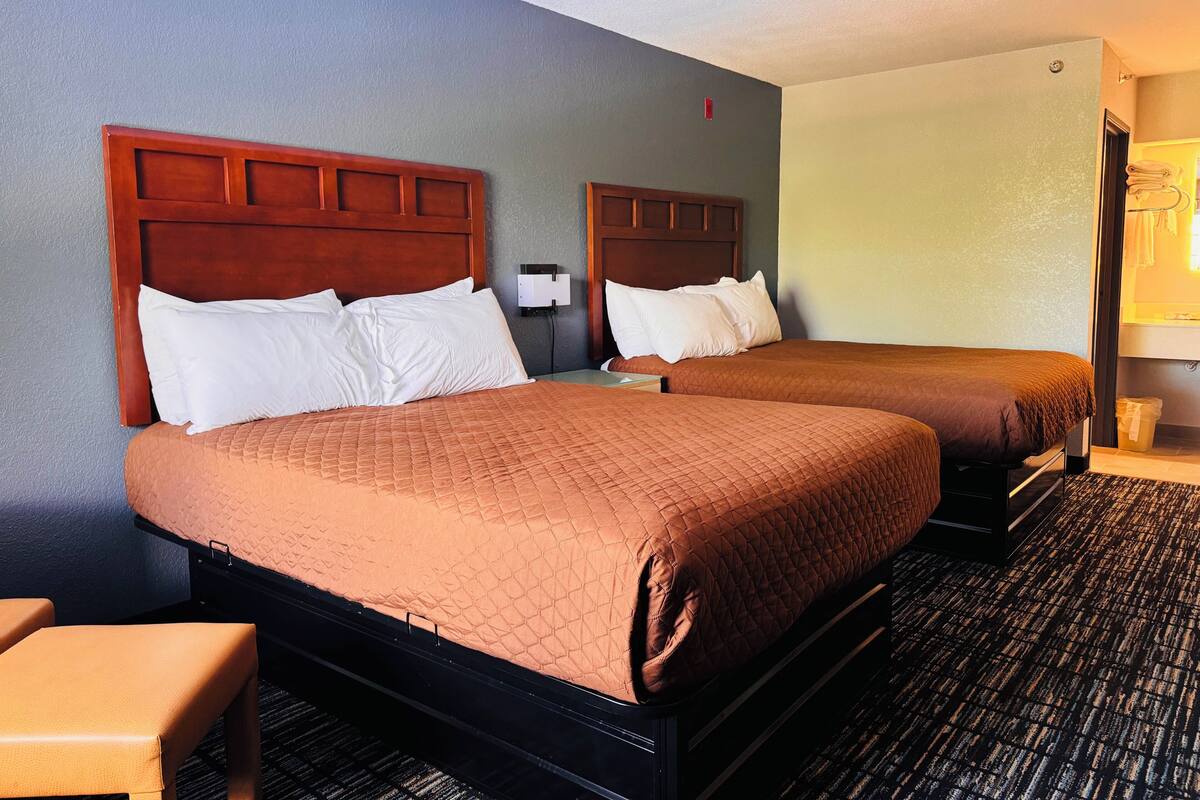A hotel room with two beds, each with a wooden headboard and white pillows.