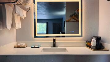 A bathroom with a large mirror, a sink, and a towel rack.