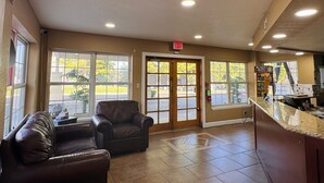 A reception area with a leather sofa, a wooden chair, a reception desk, and a door with an exit sign. - Wander Inn (Branson)