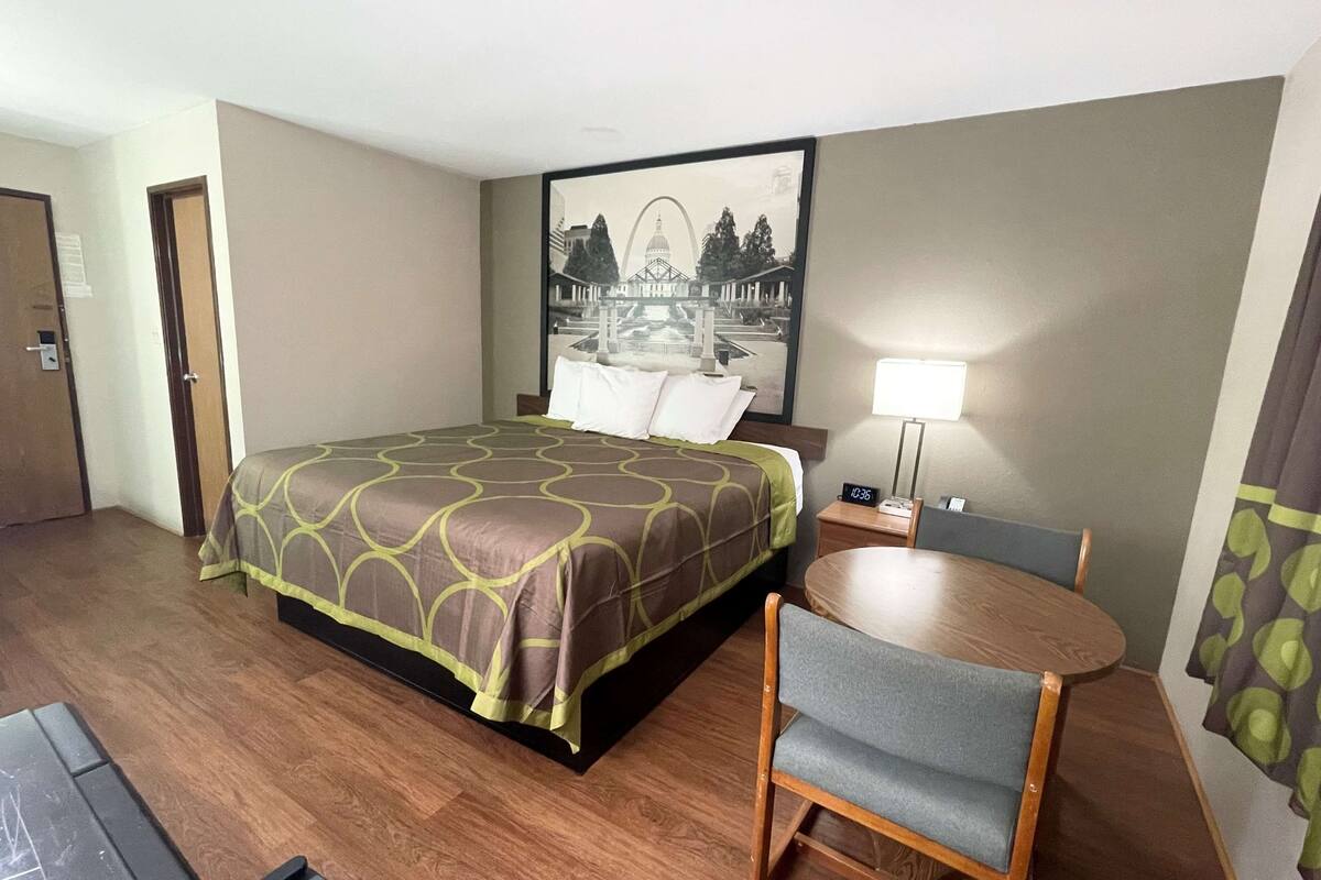 Une chambre d’hôtel avec un lit, un bureau, une chaise, une lampe et un tableau au mur.