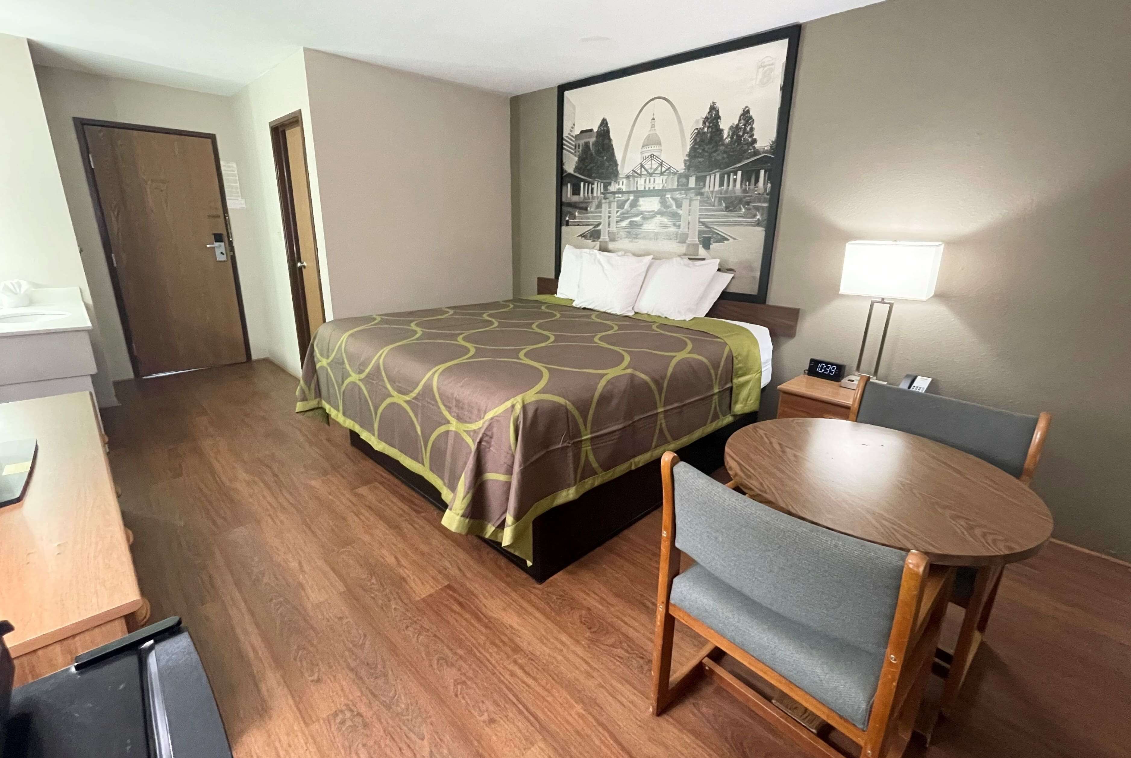 Una habitación de hotel con cama, escritorio, silla, lámpara y un cuadro en la pared.