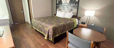 Una habitación de hotel con cama, escritorio, silla, lámpara y un cuadro en la pared.
