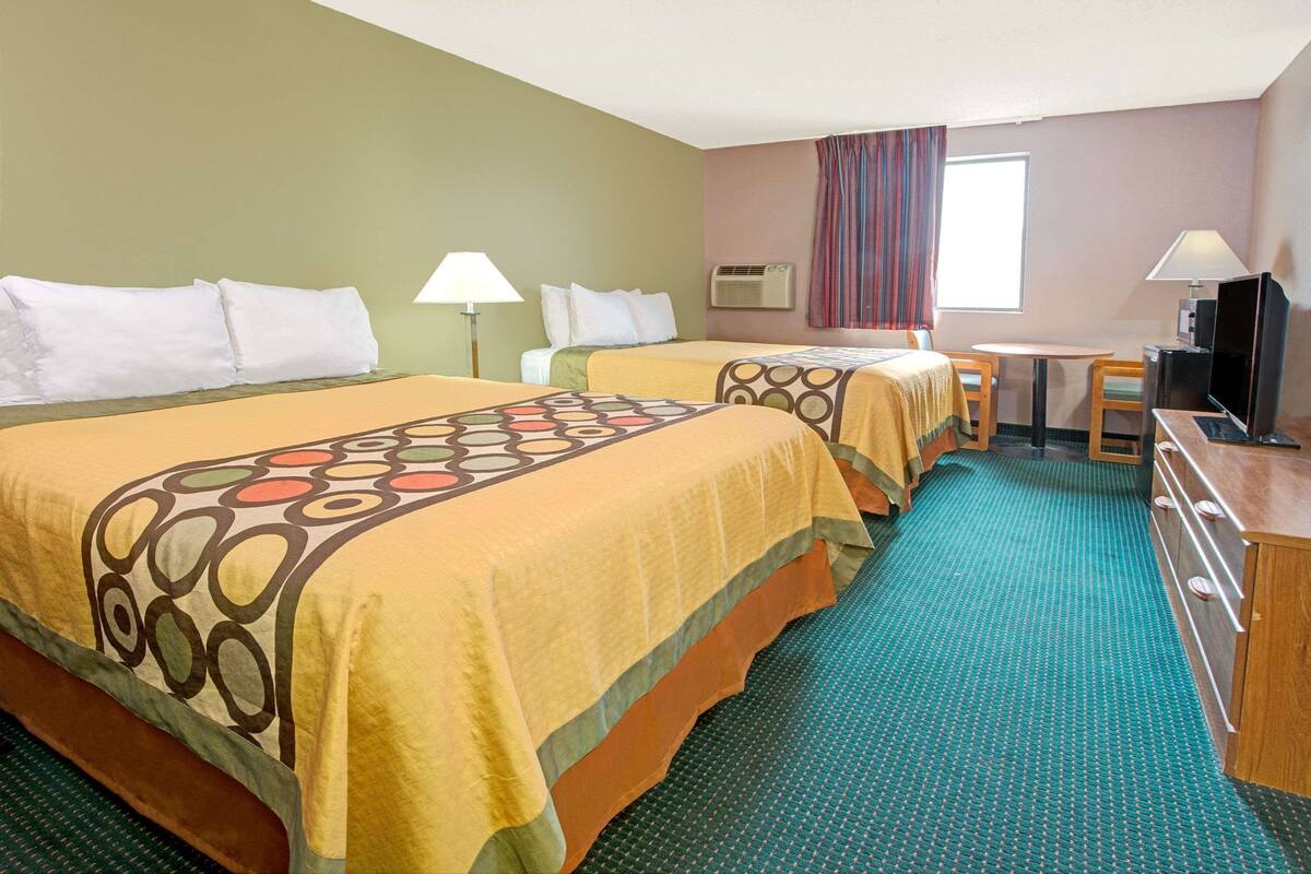 Une chambre d’hôtel avec deux lits, un bureau, une télévision et une fenêtre avec des rideaux.
