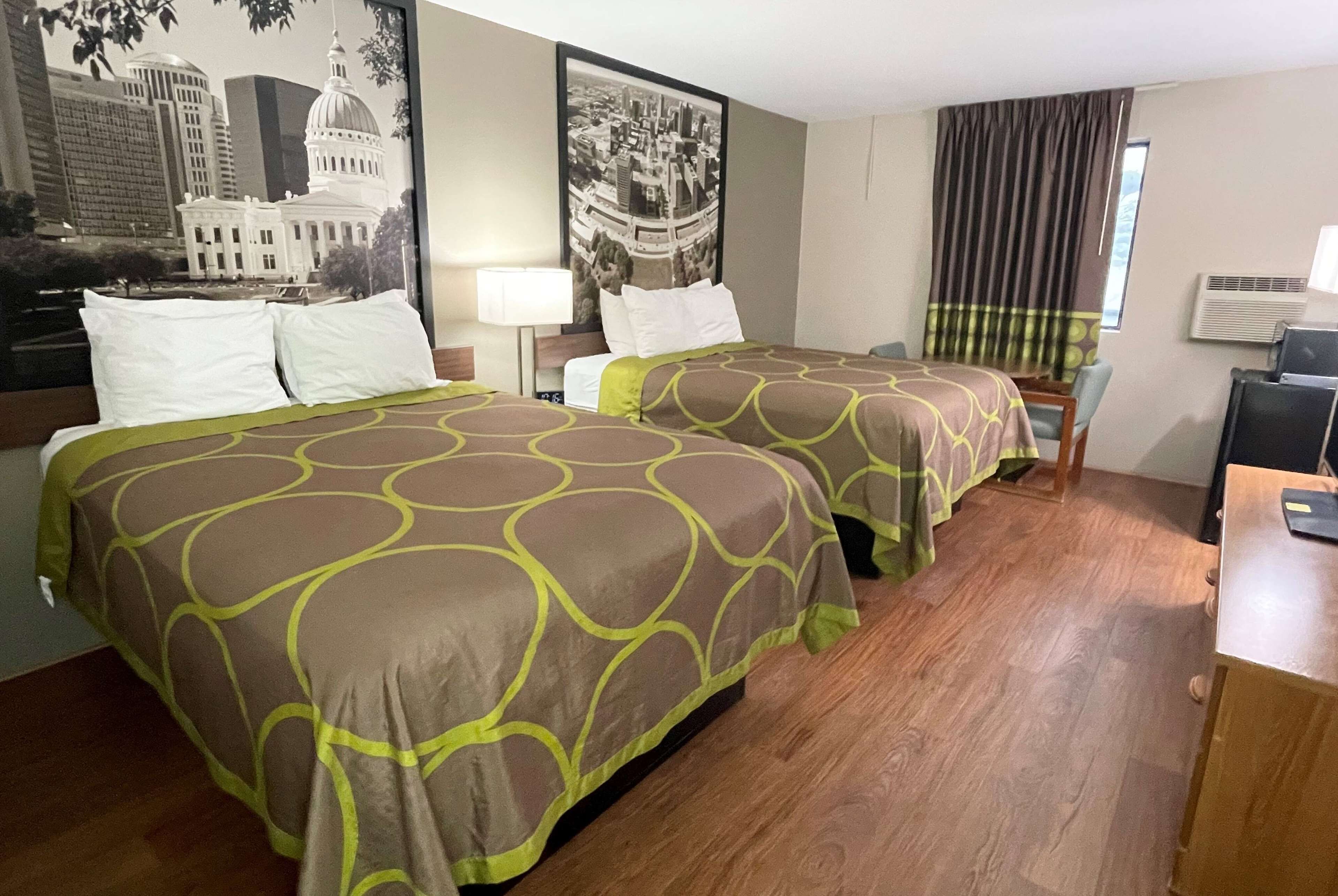 A hotel room with two beds, a desk, a chair, and a large window with curtains.