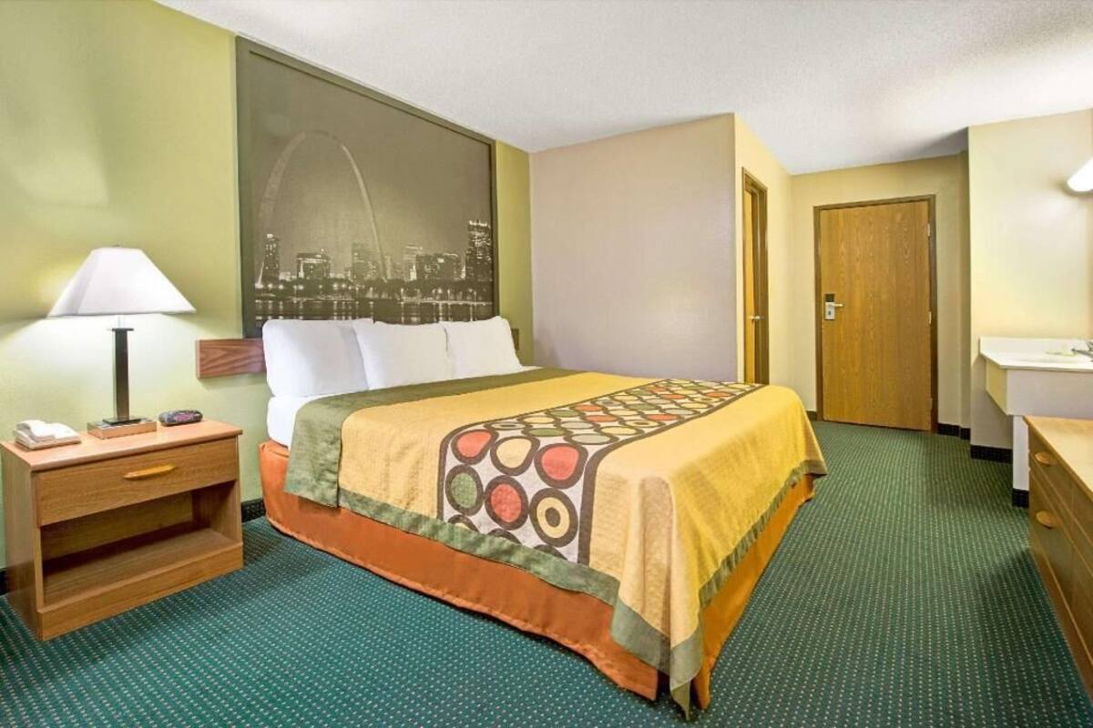 Une chambre d’hôtel comprenant un lit, une table de chevet, une lampe, une vue sur la ville, une porte et une salle de bain.