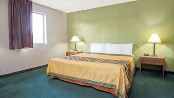 A hotel room with a bed, two bedside tables with lamps, a window with curtains, and a green wall.