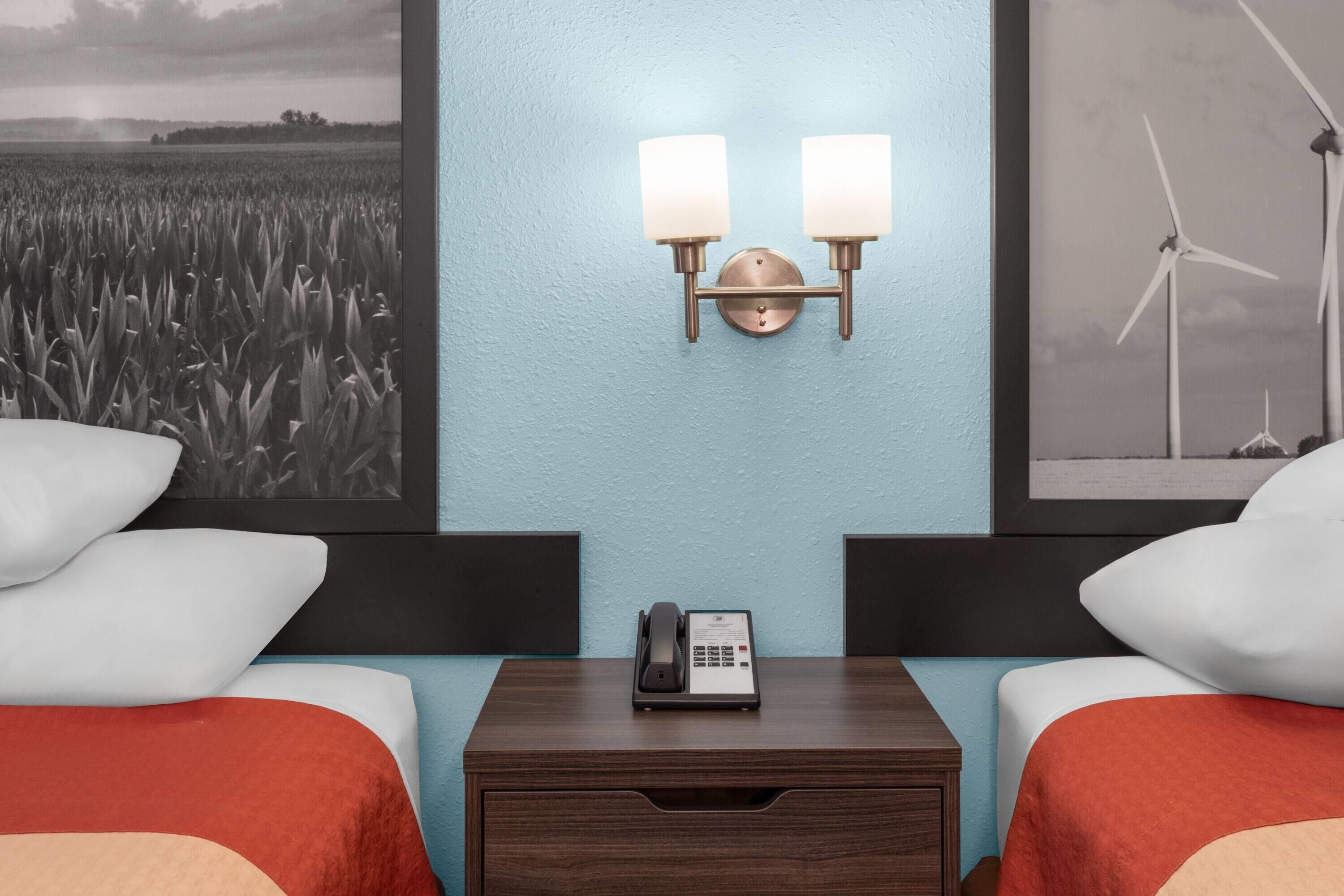 Habitación de hotel con dos camas, una mesita de noche con teléfono y luces fijadas a la pared.