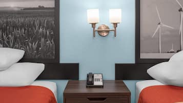 Habitación de hotel con dos camas, una mesita de noche con teléfono y luces fijadas a la pared.