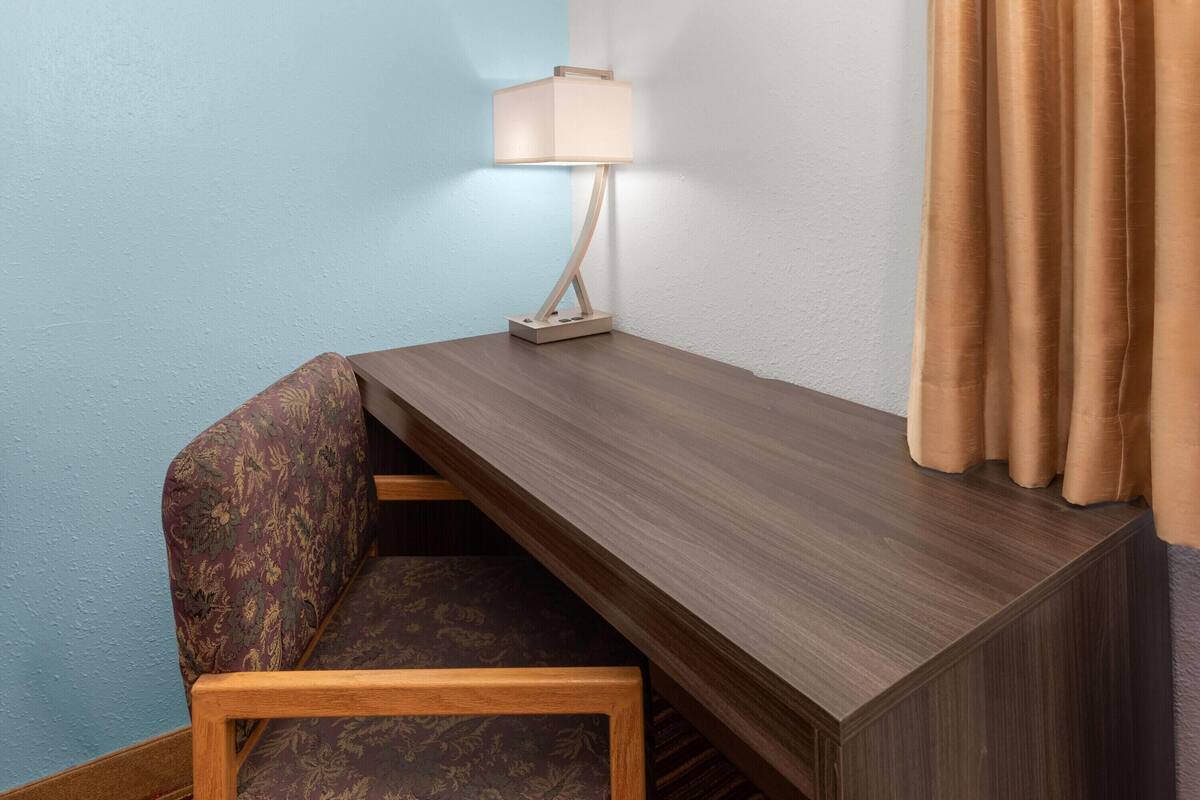 Un bureau d’angle avec une lampe, une chaise à motifs et un rideau.