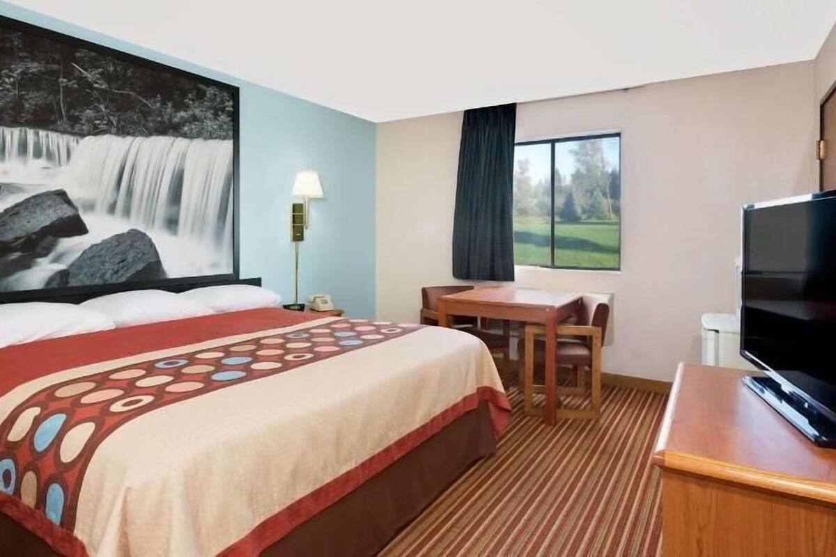 Une chambre d’hôtel équipée d’un lit, d’un bureau, d’une chaise, d’une télévision et d’une grande fenêtre.