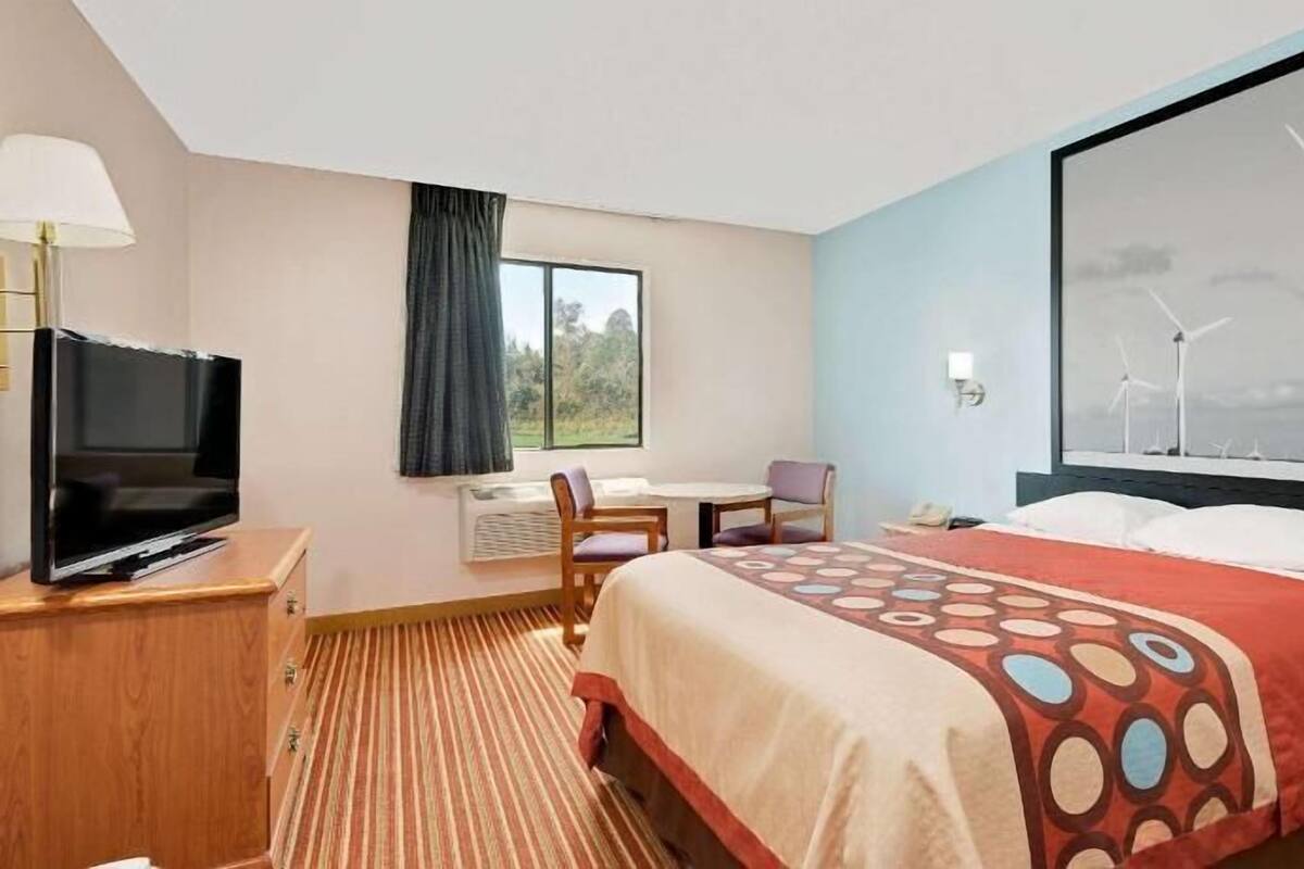 Une chambre d’hôtel équipée d’un lit, d’un bureau, d’une chaise, d’une télévision et d’une fenêtre donnant sur des éoliennes.