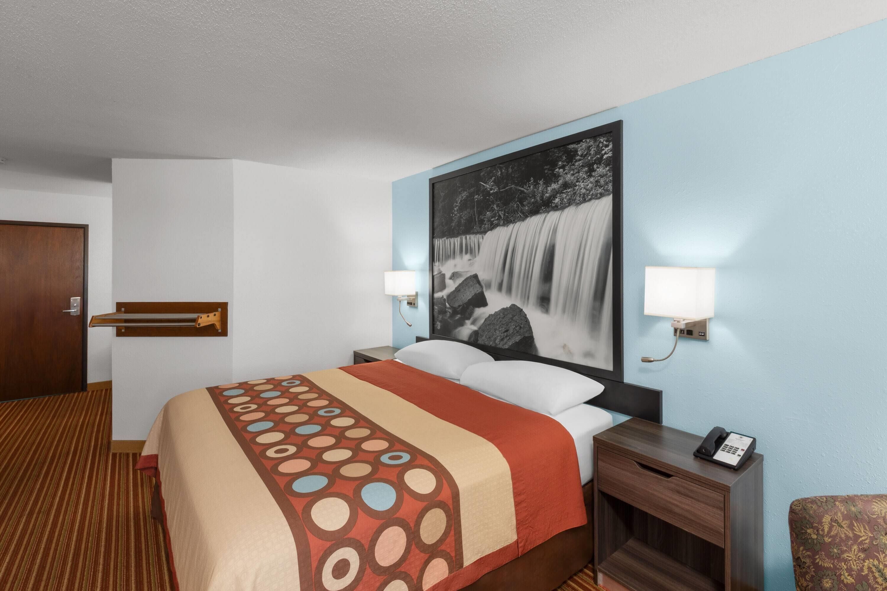 Una habitación de hotel con cama, mesita de noche, teléfono y lámpara de pared.
