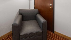 Una habitación en esquina con un sillón gris, una puerta de madera y una lámpara de pie.