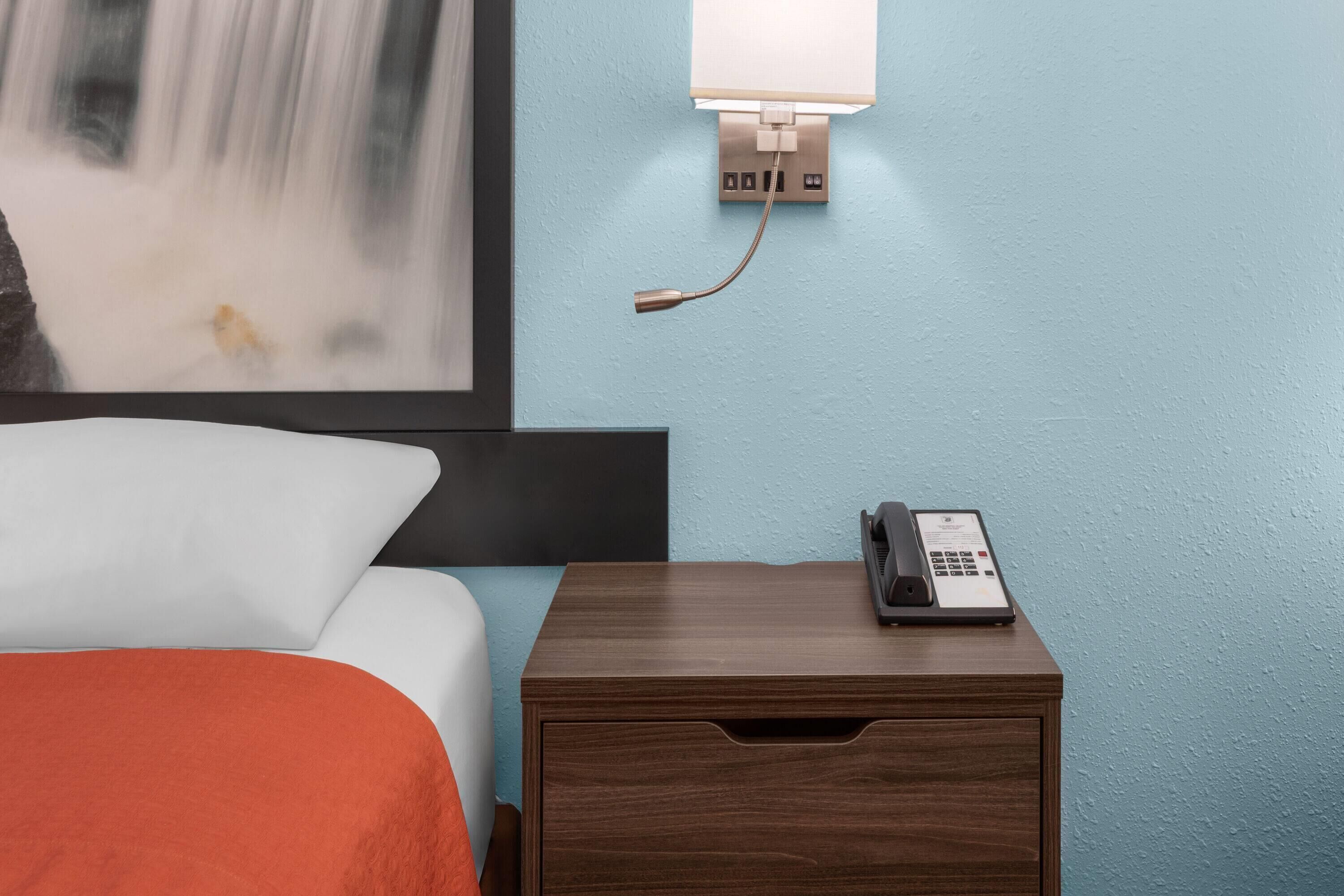 A hotel room with a bed, a nightstand with a telephone, and a wall-mounted light fixture.
