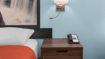 A hotel room with a bed, a nightstand with a telephone, and a wall-mounted light fixture.
