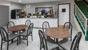 Una cocina moderna con encimeras de granito, armarios blancos y una barra desayunadora. Hay dos mesas redondas con sillas, y una escalera con barandilla verde.