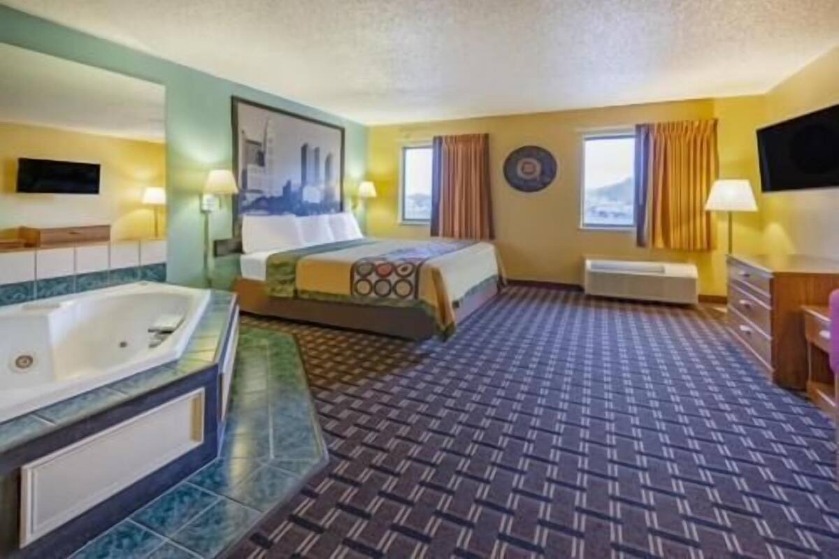 A hotel room with a large bed, a separate bathroom with a bathtub, a flat-screen TV, and a window with curtains.