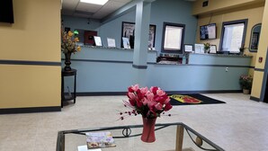 A reception area with a reception desk, a glass table with a vase of flowers, and a bulletin board with various notices. - Super 8 by Wyndham Newcomerstown (Newcomerstown)