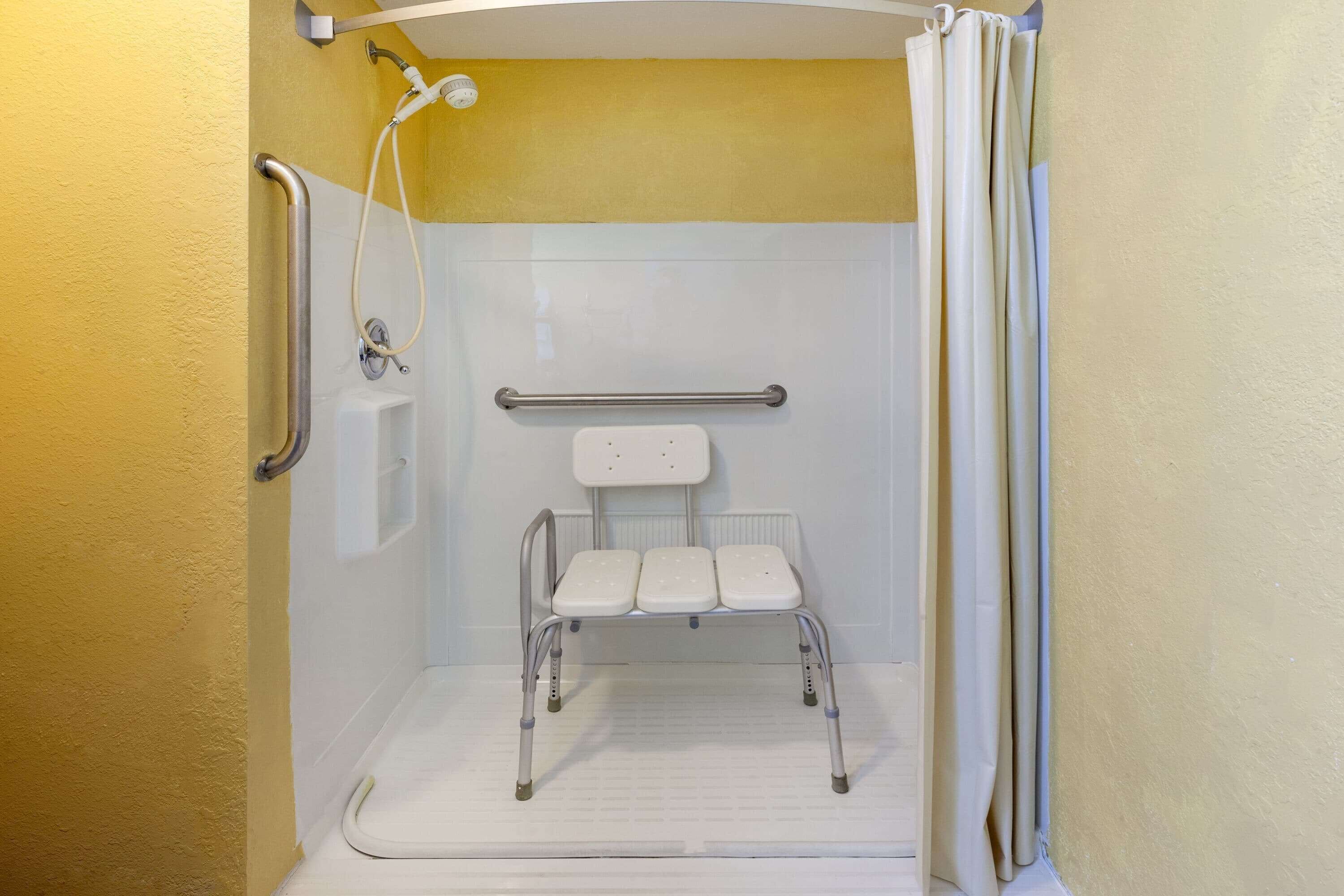 Eine barrierefreie Dusche mit Haltegriff, Duschkopf und Sitzgelegenheit.