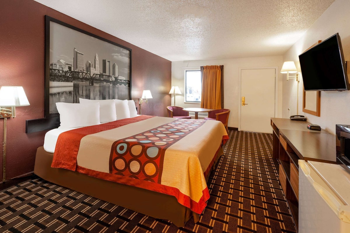 A hotel room with a large bed, a desk, a chair, a television, and a window with curtains.