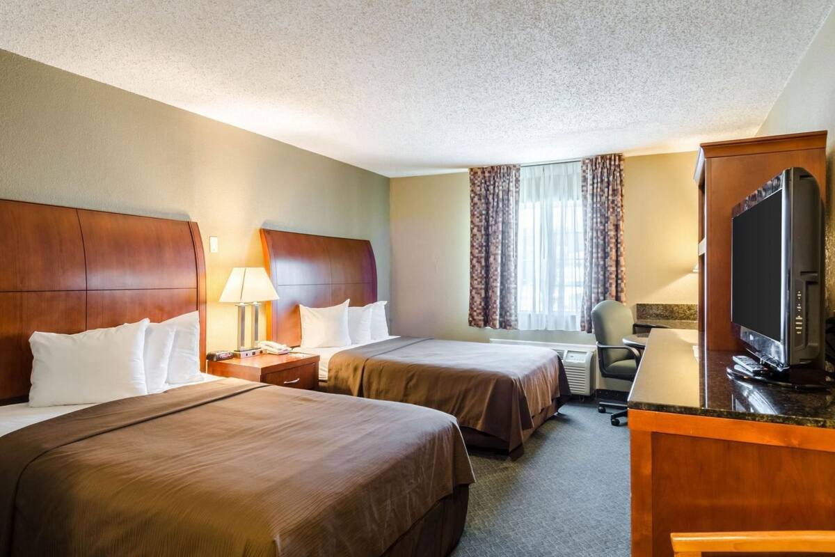 A hotel room with two beds, a desk with a television, a chair, and a window with curtains.