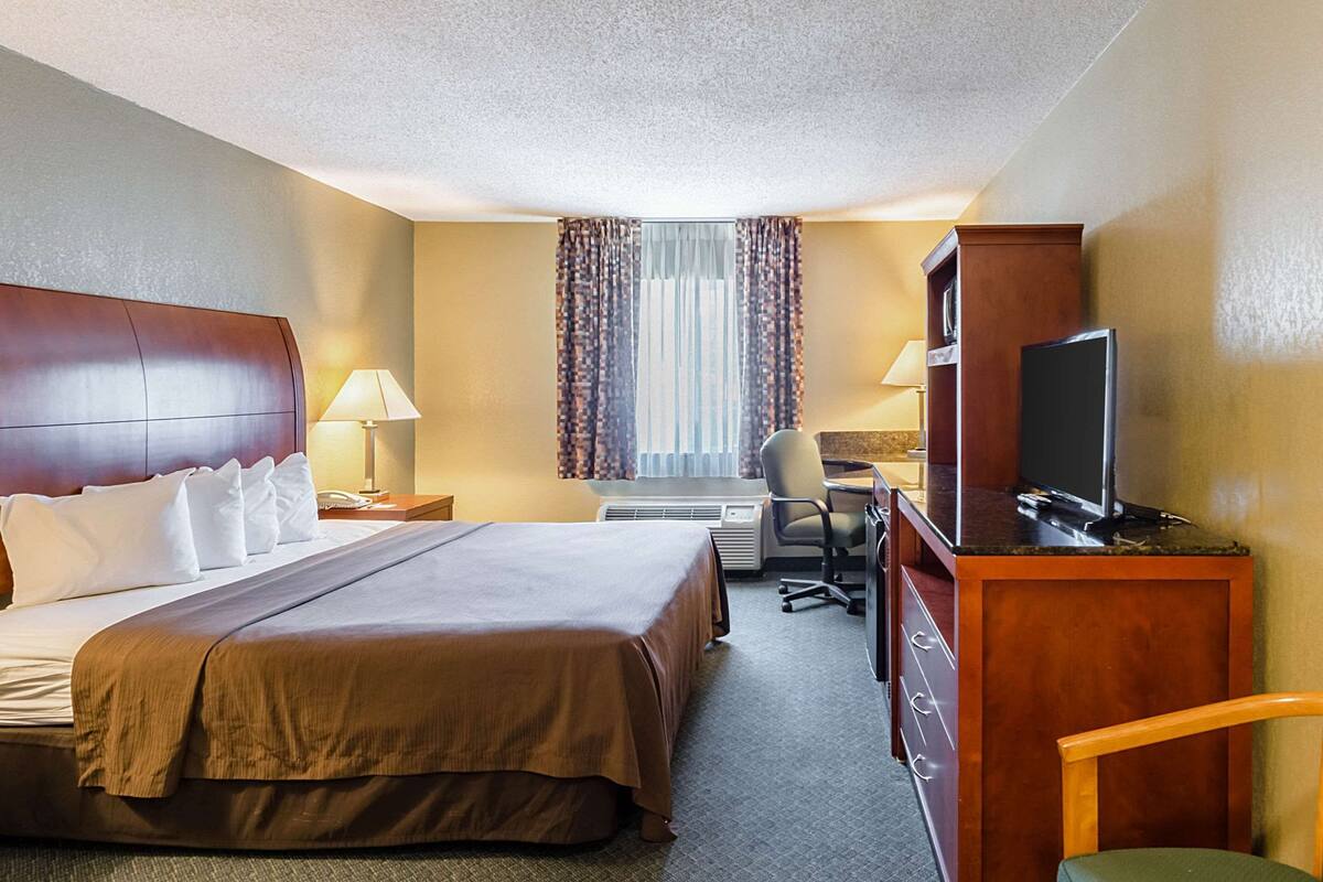 A hotel room with a large bed, a desk with a computer, a TV, and a chair.