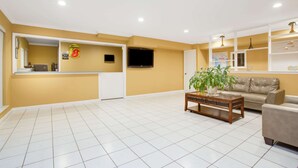A spacious living area with a sofa, a coffee table, and a television mounted on the wall. - Super 8 by Wyndham Defuniak Springs (De Funiak Springs)