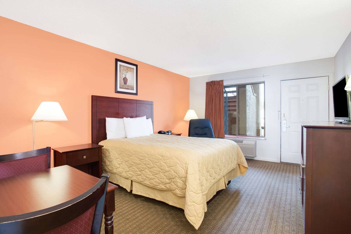 A hotel room with a bed, two bedside tables, a desk, a chair, a television, and a window with curtains.