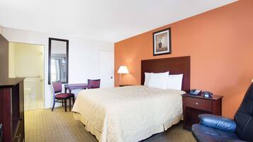 A hotel room with a bed, a desk, a chair, a nightstand, and a large mirror.